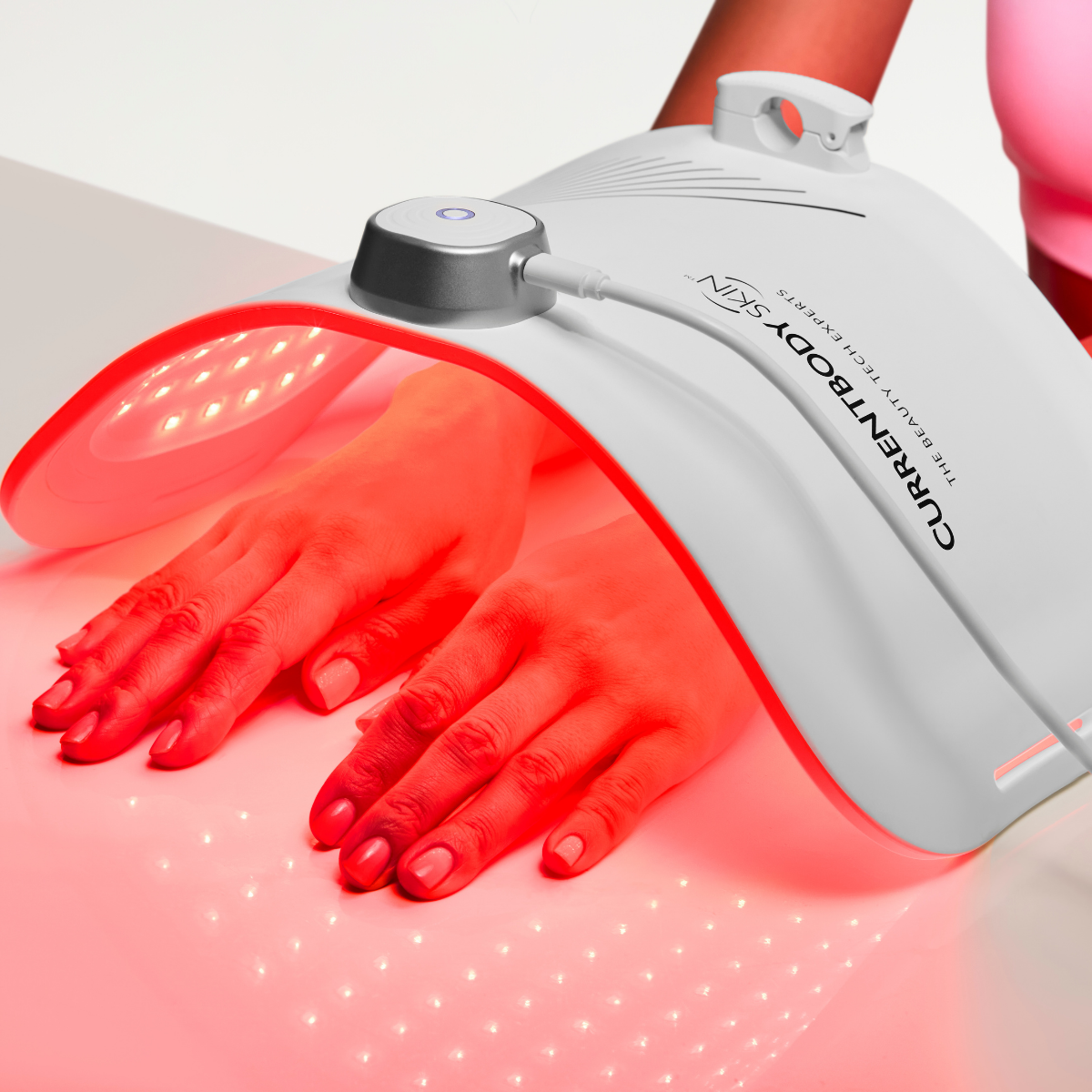 CurrentBody Skin LED light therapy panel emitting red light on hands, used for skin rejuvenation and facial skin treatment.